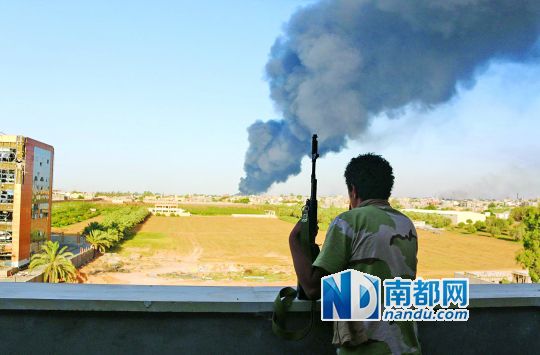 2日，利比亞首都的黎波里，一民兵武裝成員眺望被火箭彈擊中的儲(chǔ)油罐冒出濃煙。