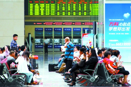 候車大廳溫度很高，一名乘客一手扇風(fēng)、一手擦汗