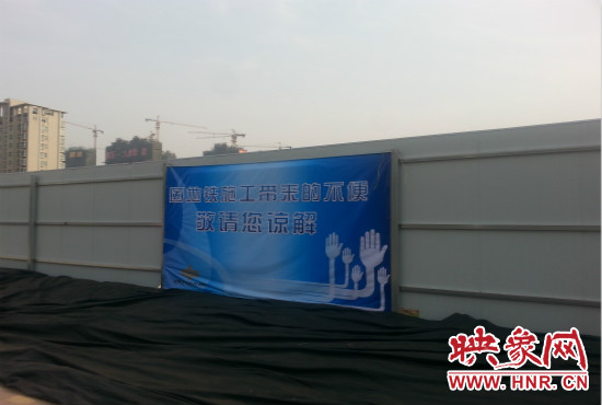道路南側(cè)圍起了白色的圍擋，墻上標(biāo)示著“因地鐵施工帶來(lái)的不便敬請(qǐng)您諒解”的提示牌。