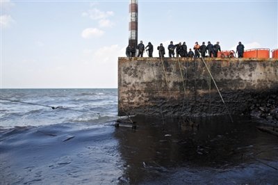 昨日，山東青島，清污人員正在海邊清理油污。
