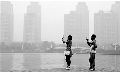 29日中午，鄭東新區(qū)如意湖畔，兩個(gè)年輕人拍攝霧霾中的景色。 鄭州晚報(bào)記者 馬健 圖