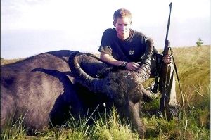 哈里王子手持獵槍，蹲在一頭遭到獵殺的水牛旁邊
