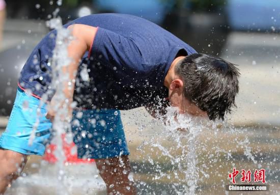 5月29日，一名小孩將頭伸向北京街頭的噴泉以降溫祛暑。