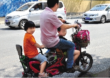 周先生騎著一輛低矮的電動車帶著一對兒女，很不安全。