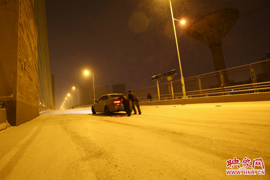 雪天路滑，汽車上橋打滑，兩名“推車人”幫助一輛私家車上坡。