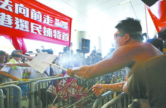17日，在香港立法會外，一名反對政改的男子向支持派人群投擲標牌。