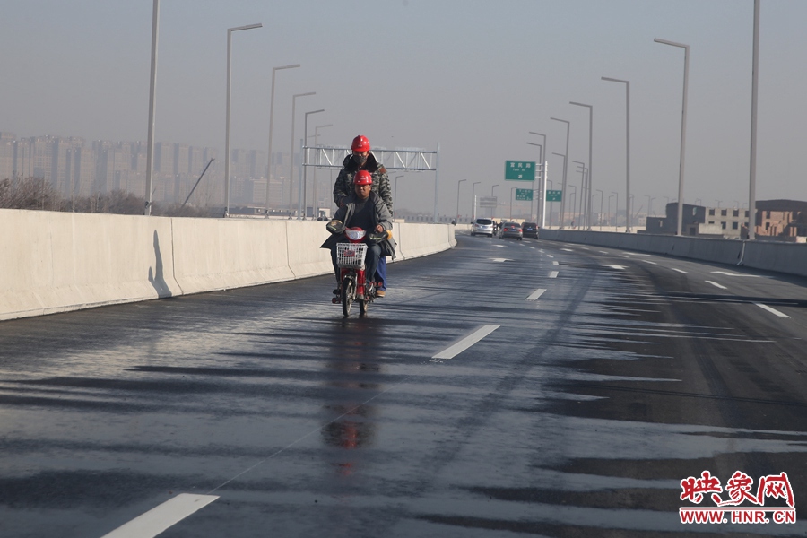兩名工人騎車經(jīng)過灑水養(yǎng)護路面。