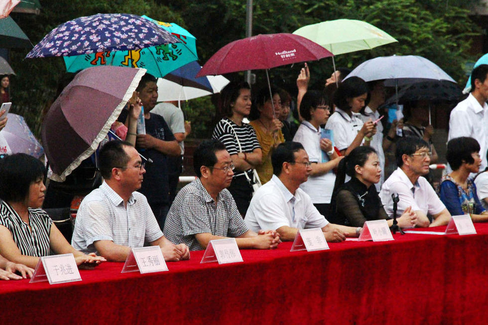 在主席臺上觀看的校領導也堅持不打傘陪學生一起淋雨，身旁站滿了打傘觀看的家長。