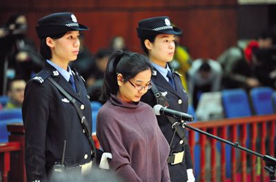 被告人盧梅低著頭，站在朝陽(yáng)法院刑事審判庭的被告席上。